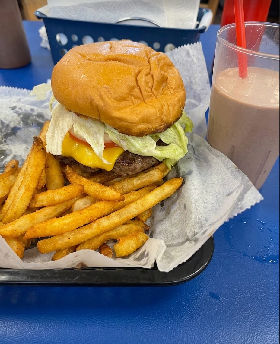 A cheeseburger with crinkle fries and a chocolate shake on a blue diner table