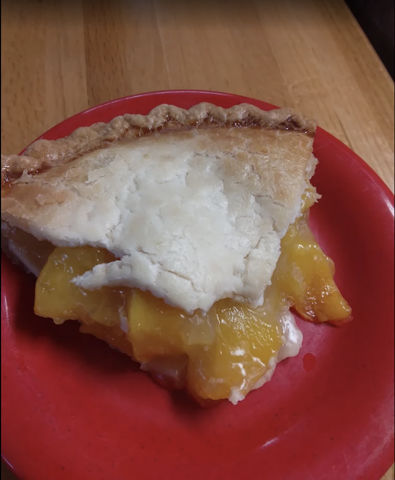 A slice of peach pie on a red plate on a wood table