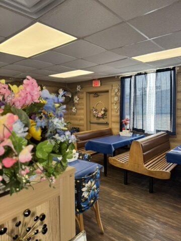 A cozy corner with wooden benches, a floral arrangement and blue tables by the window