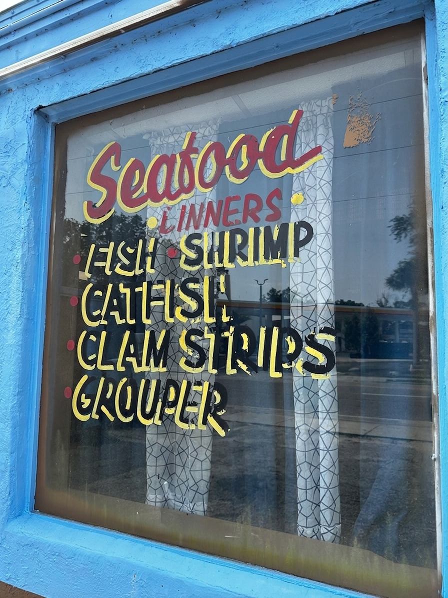 Barbara's hand-painted 'Seafood Dinners' window sign listing fish, shrimp, catfish, clam strips and grouper